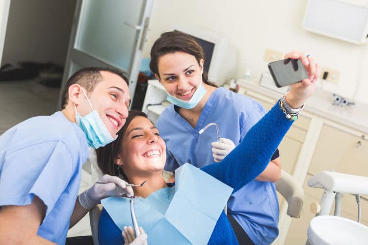 Consultório odontológico e dentista fazendo selfie com paciente cumprindo as regras do CFO, através das 5 dicas para atrair pacientes nas redes sociais.